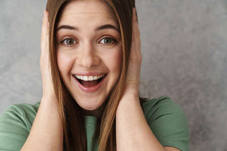 Close up of a happy blonde young woman gesturing over gray wall, cover ears