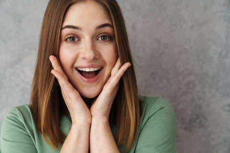 Close up of a happy blonde young woman gesturing over gray wallの写真素材