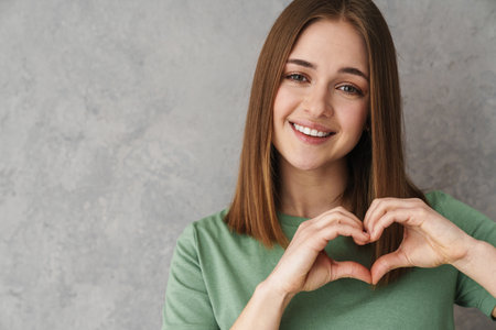 Happy beautiful nice girl showing heart gesture and smiling isolated over grey wallの写真素材
