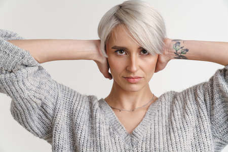 White-haired young woman posing with hands clasped behind her neck isolated over white wallの写真素材