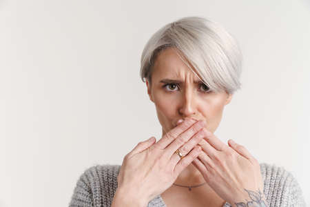 Displeased silver girl covering her mouth and looking at camera isolated over white backgroundの写真素材
