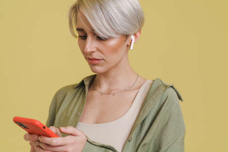 Young grey woman listening with cellphone and earphones isolated over beige backgroundの写真素材