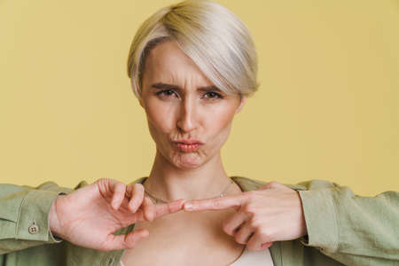 Young white-haired woman frowning and holding fingers together isolated over beige backgroundの写真素材