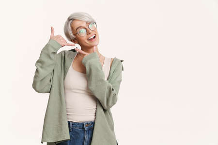 Smiling girl pointing finger aside while showing handset gesture isolated over white background