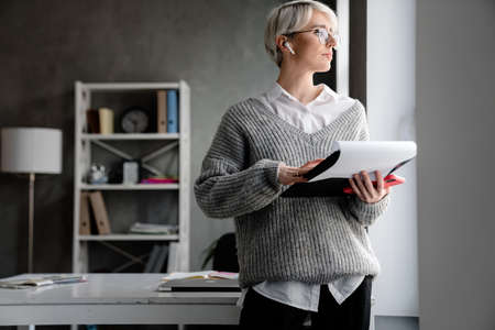 White-haired focused woman using earphone while examining documents in office
