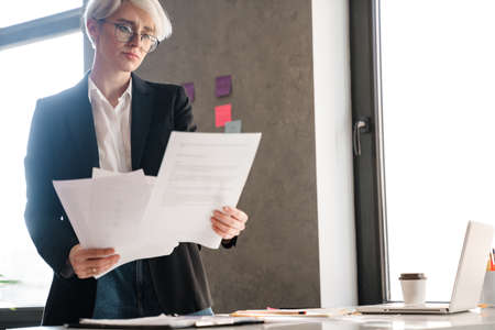 White-haired focused woman working with papers and laptop in officeの写真素材