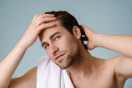Brunette bearded shirtless man with towel over blue wall, posingの写真素材