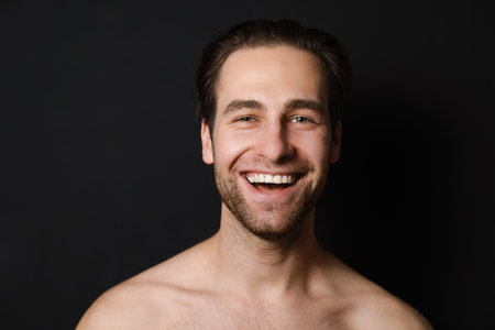 Shirtless white man laughing and looking at camera isolated over black wall