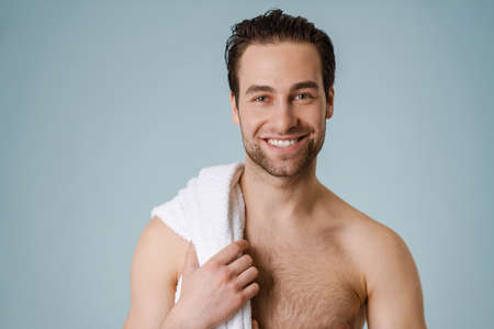 Happy brunette bearded shirtless man with towel over blue wallの写真素材