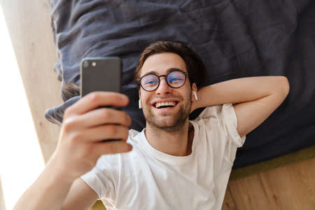Smiling mid aged brunette man taking a selfie while laying on a floor at homeの写真素材