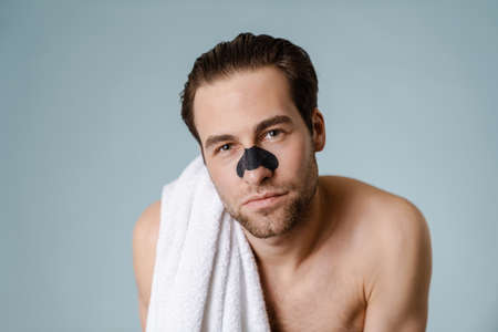 Close up of a brunette shirtless man with stubble wearing nose patch against blackheads standing...