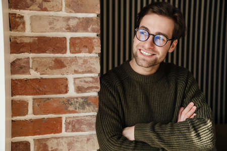 Smiling mid aged brunette man in leaning on a brick wall indoorsの写真素材