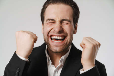 Unshaven excited man in jacket screaming and making winner gesture isolated over white background