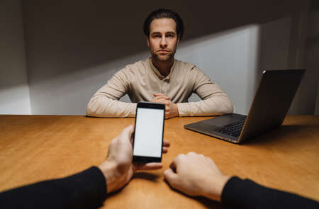 Serious brunette entrepreneur sitting in the office during interview with a boss, holding blank screen mobile phoneの写真素材