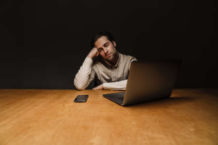 Serious pensive brunette businessman working on laptop computer in dark office