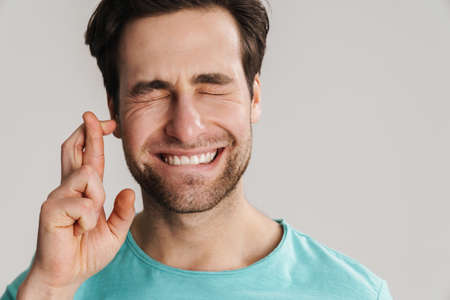 Young man making a wish isolated on gray background, holding fingers crossed, close upの写真素材