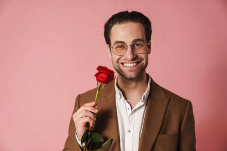 Happy mid aged brunette man in jacket holding red rose over pink wall backgroundの写真素材