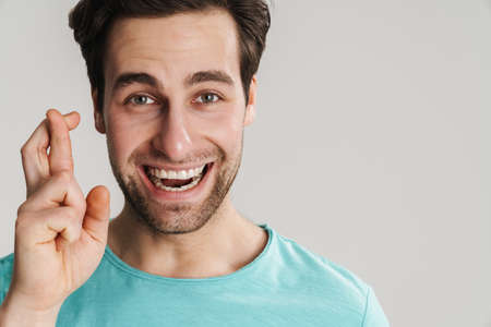 Young man making a wish isolated on gray background, holding fingers crossed, close up