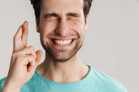 Young man making a wish isolated on gray background, holding fingers crossed, close upの写真素材