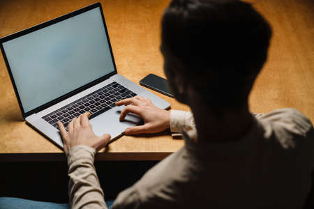 Serious pensive brunette businessman working on laptop computer in dark officeの写真素材