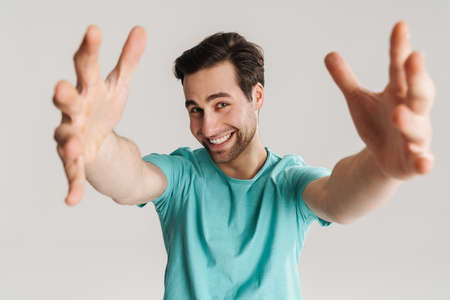 Joyful handsome guy smiling and reaching out hands to camera isolated over white wallの写真素材
