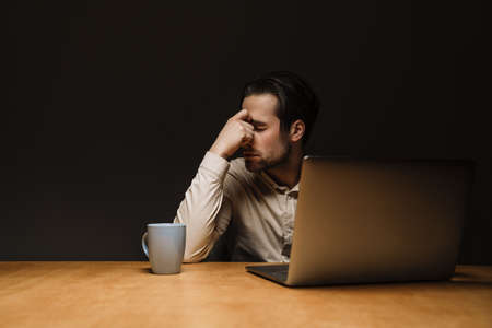 Serious pensive brunette businessman working on laptop computer in dark office