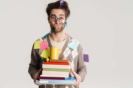 Shocked nerdy man holding stack of books isolated over gray background