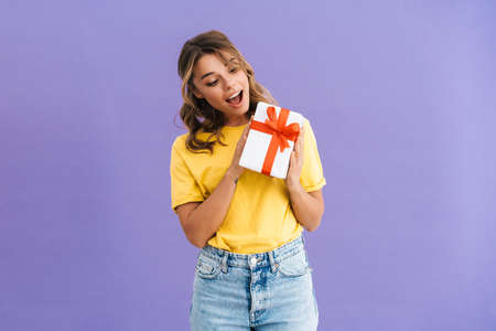 Happy excited young woman showing present box isolated over blue backgroundの写真素材