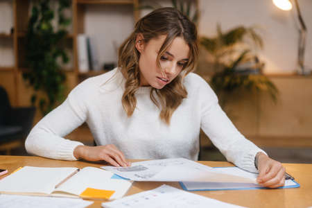 Beautiful young woman entrepreneur working with documents while sitting at the office deskの写真素材