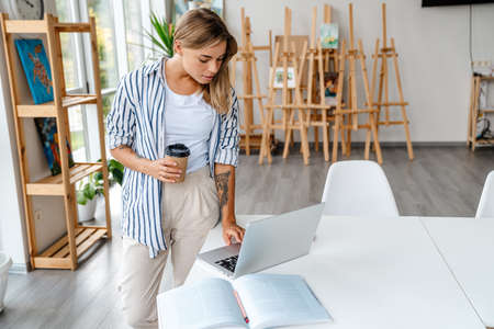Attractive confident young woman designer working at the studio office workshop, using laptop,...