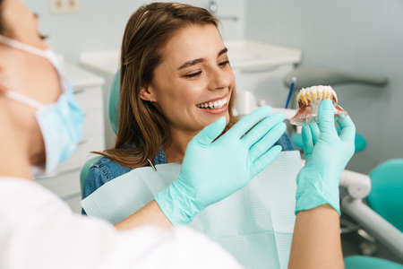 Dentist woman showing teeth imitation to her smiling patient in dental clinic