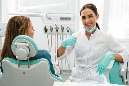 European mid dentist woman showing thumb up while working with patient in dental clinicの写真素材