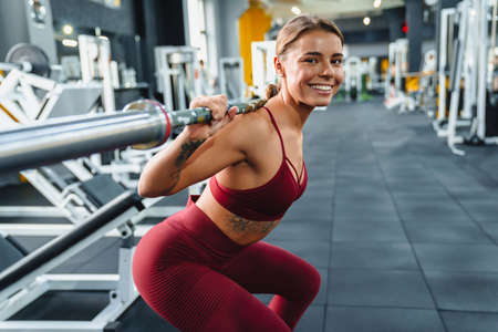Happy athletic sportswoman doing exercise with barbell while working out in gym