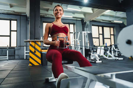 Smiling athletic sportswoman doing exercise on fitness equipment while working out in gym