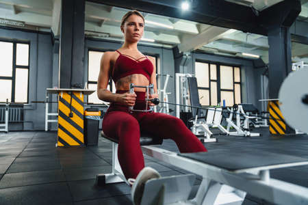 Focused athletic sportswoman doing exercise on fitness equipment while working out in gym