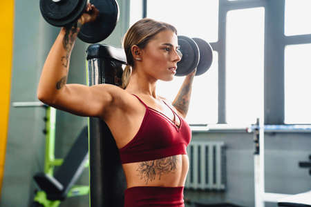 Image of concentrated serious young woman fitness coach making sport exercise for arms with...