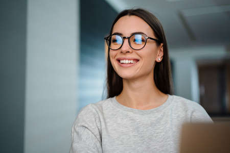 Happy young woman in eyeglasses smiling while working with laptop at homeの写真素材