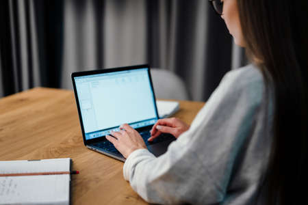 Brunette focused young woman in eyeglasses working with laptop at homeの写真素材