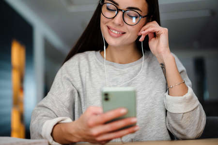 Happy young woman listening music with earphones and mobile phone while sitting at homeの写真素材