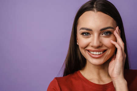 Happy beautiful brunette girl smiling and looking at camera isolated over purple backgroundの写真素材