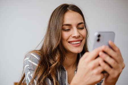 Happy beautiful woman smiling and using cellphone while sitting at home