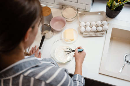 Caucasian brunette woman making pancake dough at home kitchen