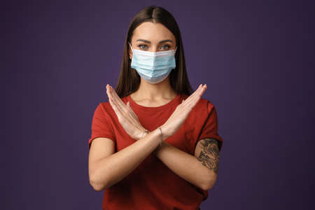 Beautiful brunette girl in protective mask showing stop gesture isolated over purple backgroundの写真素材