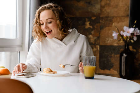 White blonde woman using mobile phone and having breakfast at homeの写真素材