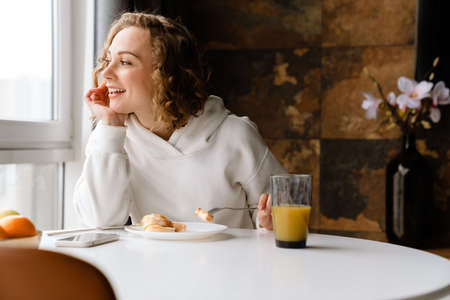 White blonde woman having breakfast while sitting at table in homeの写真素材