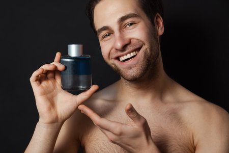 Shirtless white man smiling while showing cologne isolated over blue wallの写真素材