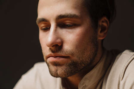 Close up of a sad upset brunette man looking down, sitting indoorsの写真素材