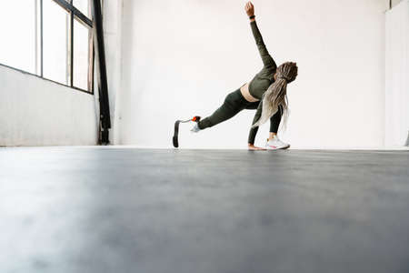 Young sportswoman with prosthesis doing exercise while working out indoors
