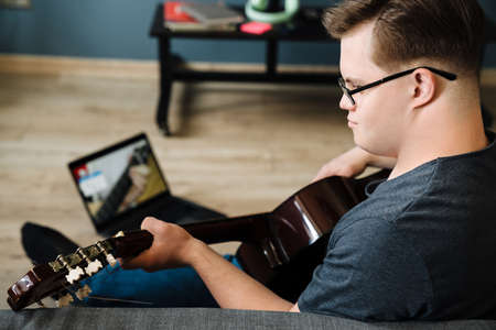 Young man with down syndrome playing guitar while using laptop at home