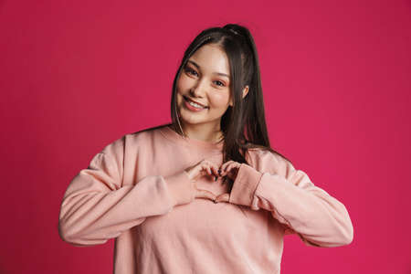 Asian brunette woman smiling and showing heart gesture isolated over purple wallの写真素材